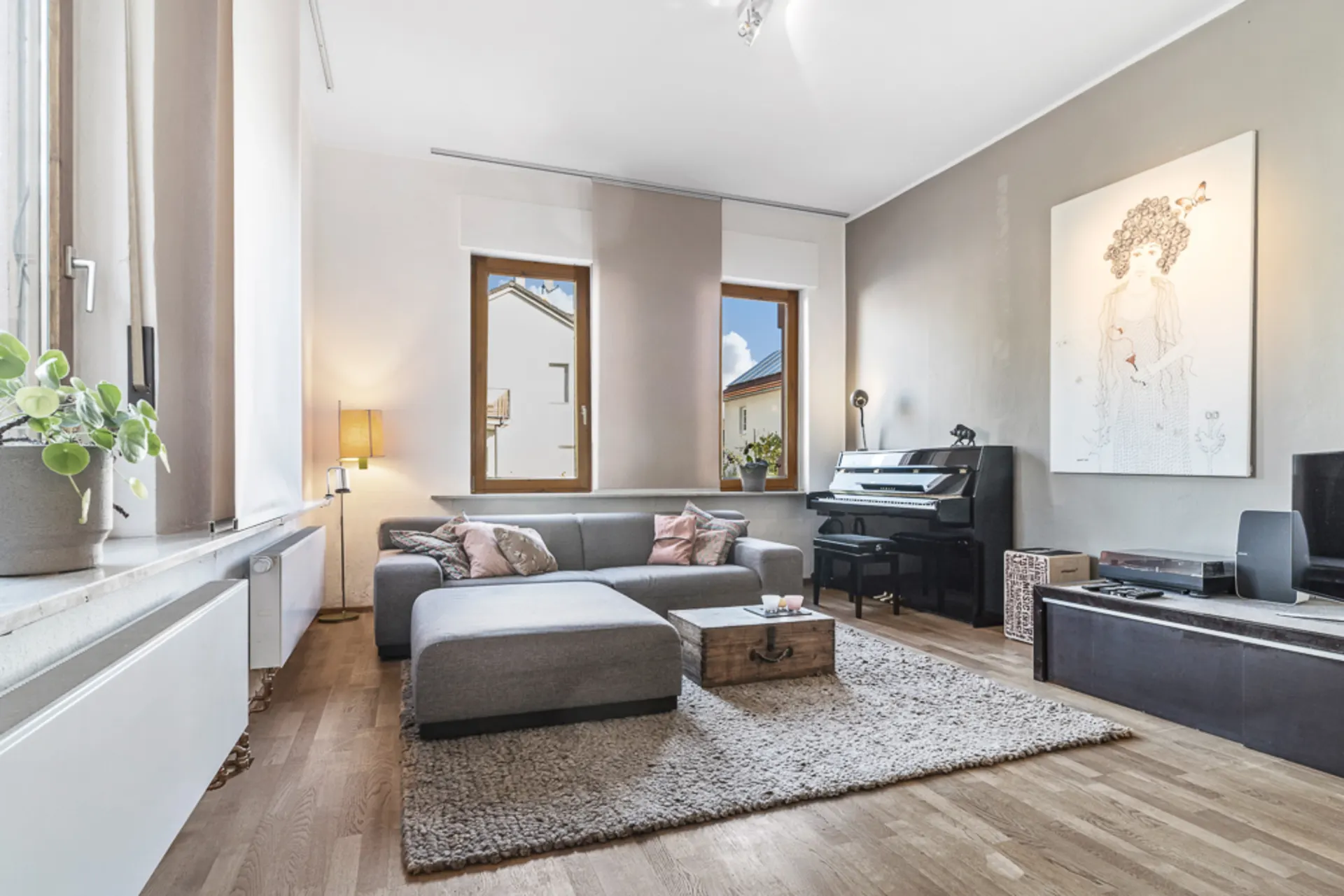 Modernes Wohnzimmer mit grauem Sofa, Teppich, Klavier und großem Wandbild.