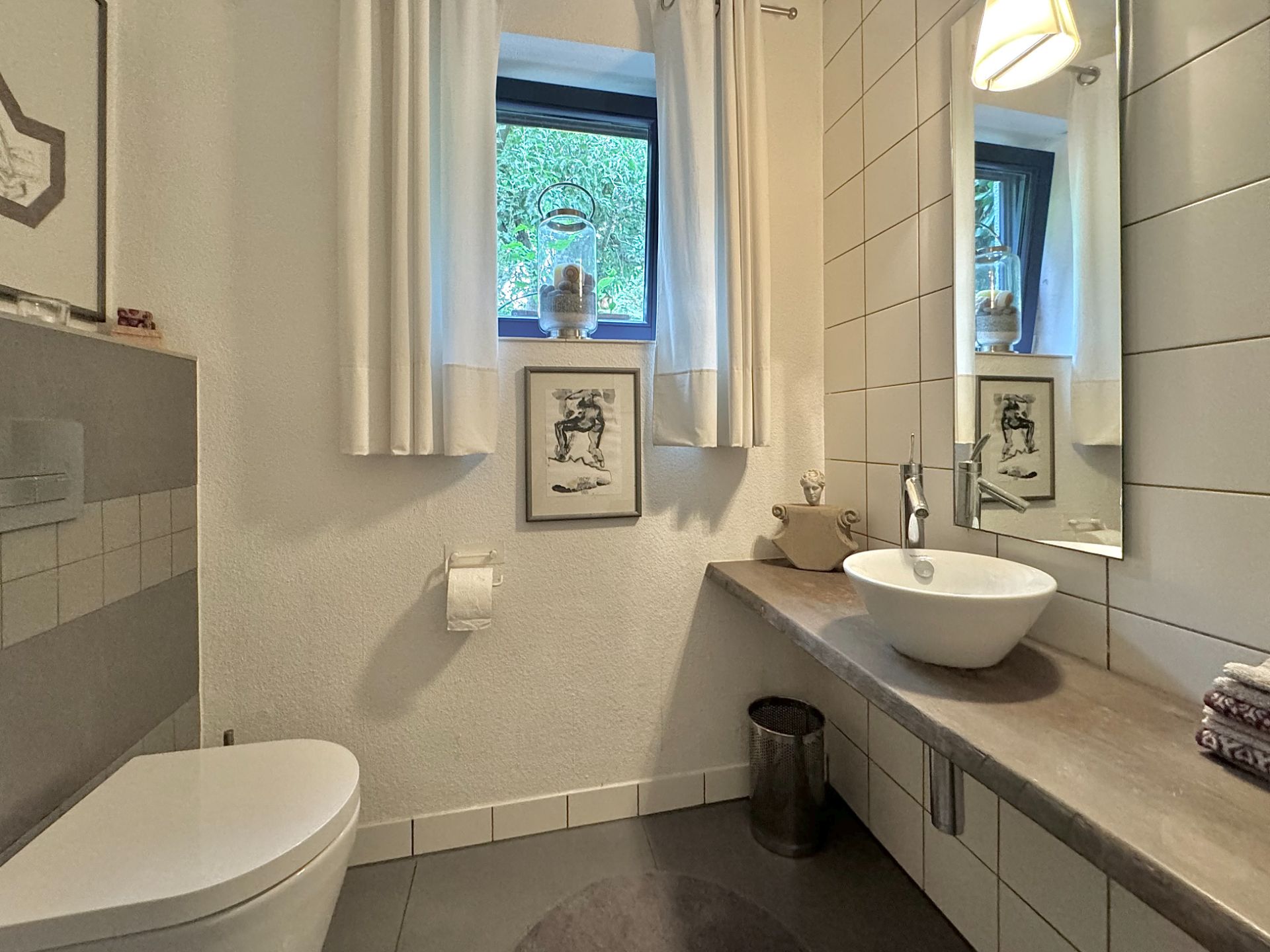 Modernes Badezimmer mit rundem Waschbecken, großem Spiegel, Fenster und Toilette.