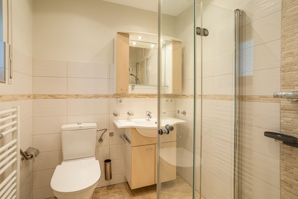 Helles Badezimmer mit Toilette, Waschbecken, Spiegel und verglaster Dusche.