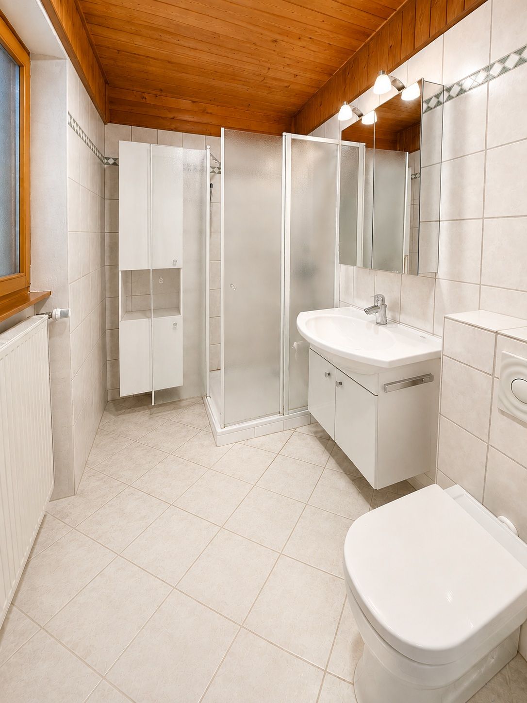 Modernes Badezimmer mit Dusche, Waschbecken, WC, Spiegelschrank und Holzbalkendecke.