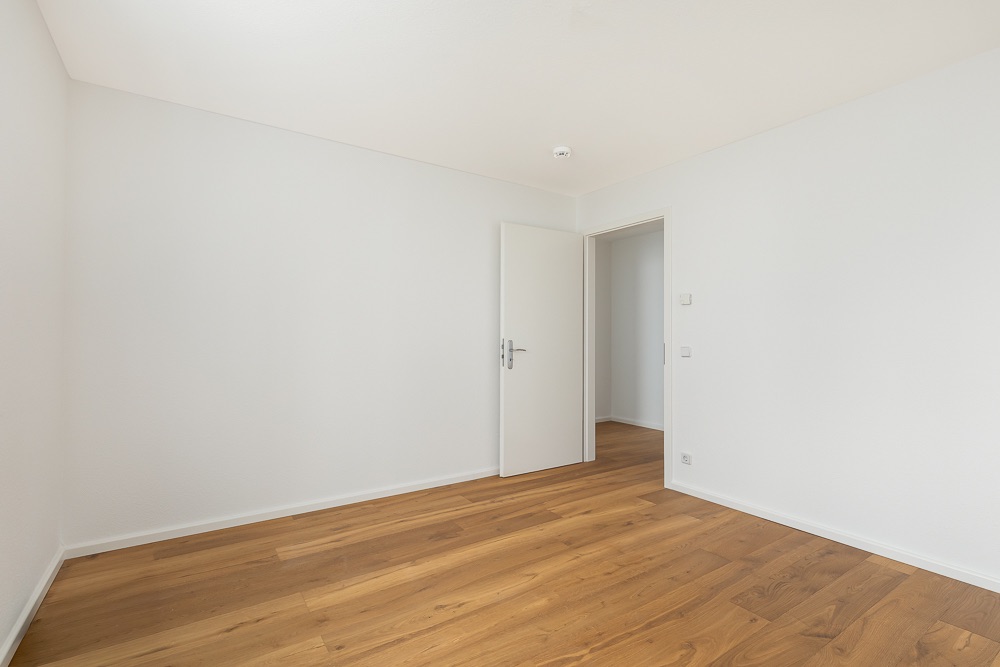 Leeres Zimmer mit weiß gestrichenen Wänden, Holzboden und geöffneter Tür.