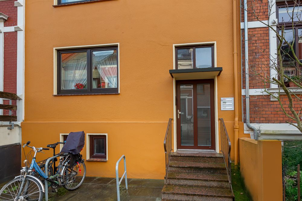 Eingangstür mit Treppe, gelbe Hauswand, Fenster und zwei Fahrräder im Vordergrund.