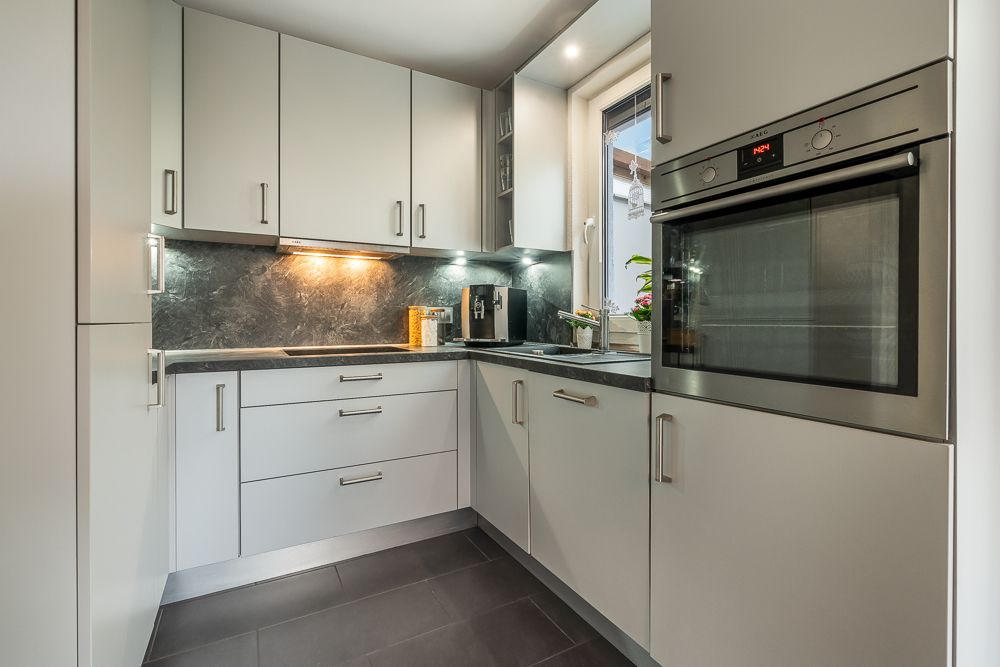 Moderne Einbauküche mit grauen Schränken, Arbeitsplatte, Backofen und Fenster.