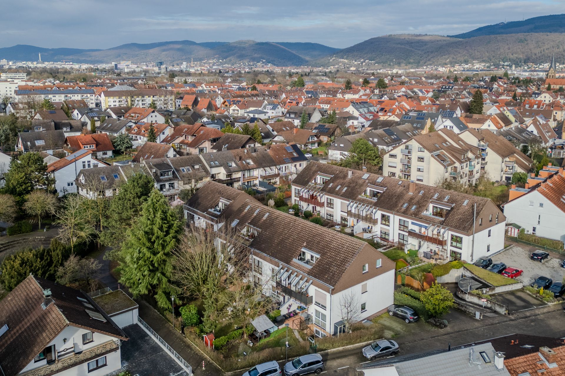 Luftaufnahme einer Wohnsiedlung mit Mehrfamilienhäusern, Gärten und parkenden Autos.