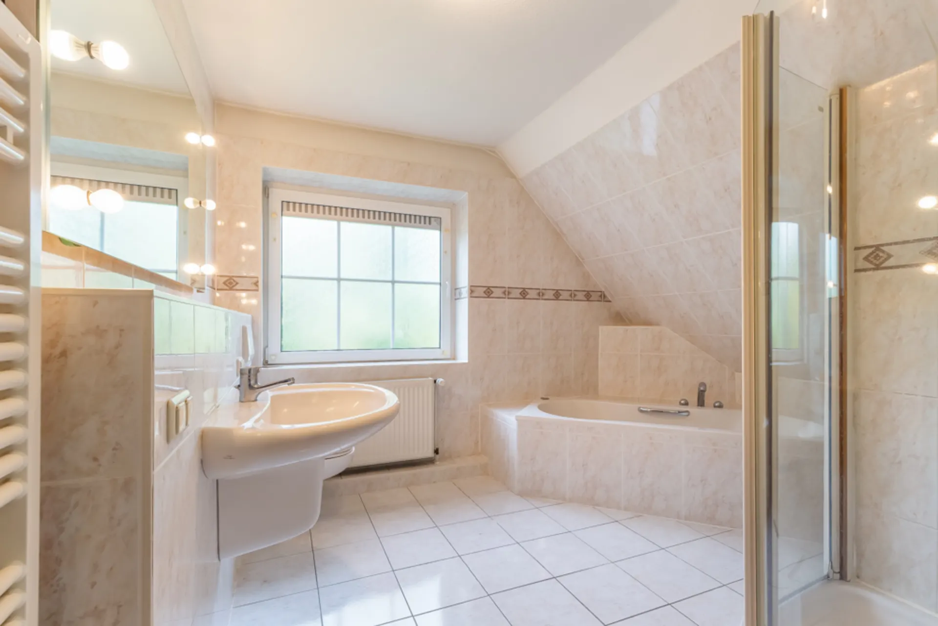 Helles Badezimmer mit Waschbecken, Badewanne, Fenster und Dusche, gefliest.