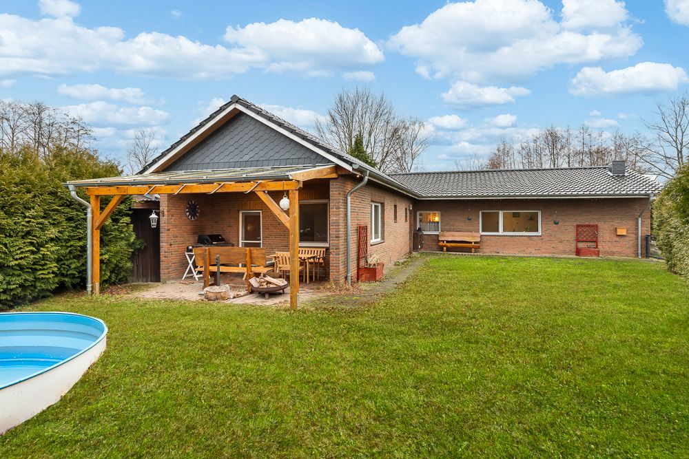 Backstein-Einfamilienhaus mit überdachter Terrasse, Garten und kleinem Pool im Freien.