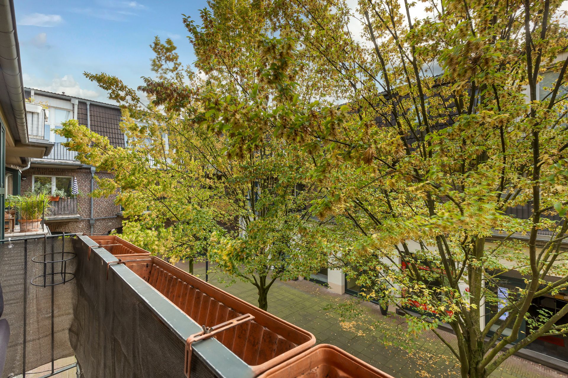 Blick von einem Balkon mit Blumenkästen auf grüne Bäume und Nachbargebäude.