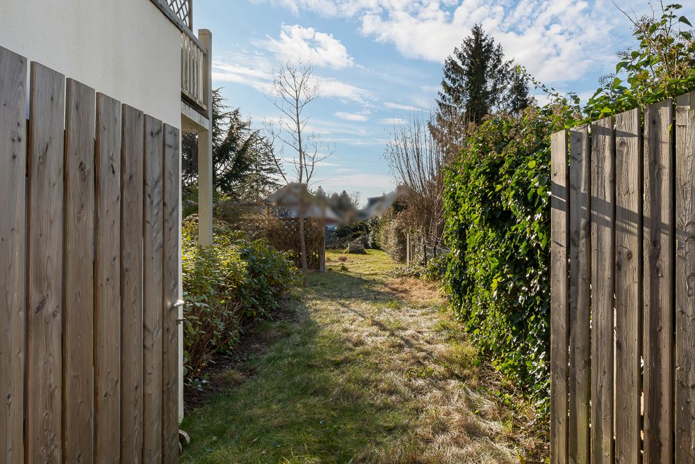 Holztor öffnet sich zu einem Gartenweg mit Gras, Büschen und Bäumen.