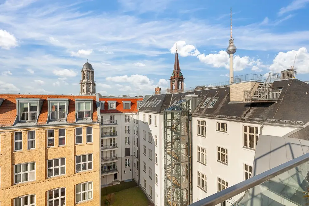 Blick von einem Balkon auf Innenhof mit mehreren Wohngebäuden und Berliner Fernsehturm im Hintergrund.