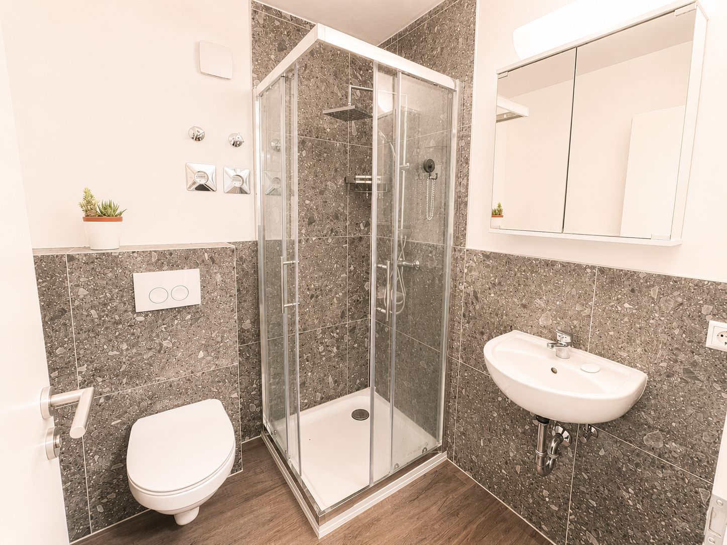 Modernes Badezimmer mit Eckdusche, Wandspiegel, Waschbecken und Toilette.