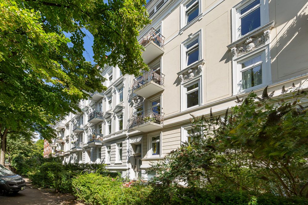 Helles Wohnhaus mit Balkonen und Bäumen im Vordergrund.