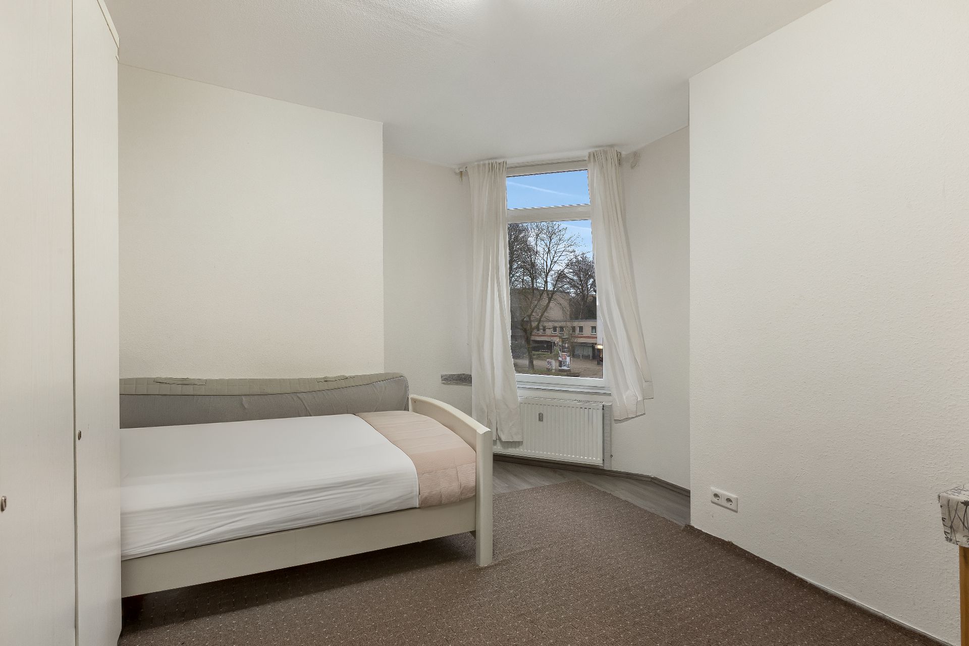Helles Schlafzimmer mit Einzelbett, Kleiderschrank und Fenster mit Blick nach draußen.