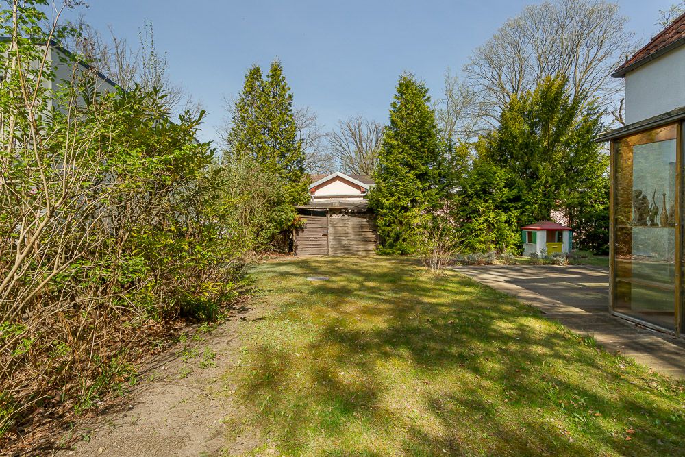 Garten mit Rasenfläche, Bäumen, kleinem Spielhaus und Holzschuppen im Hintergrund.