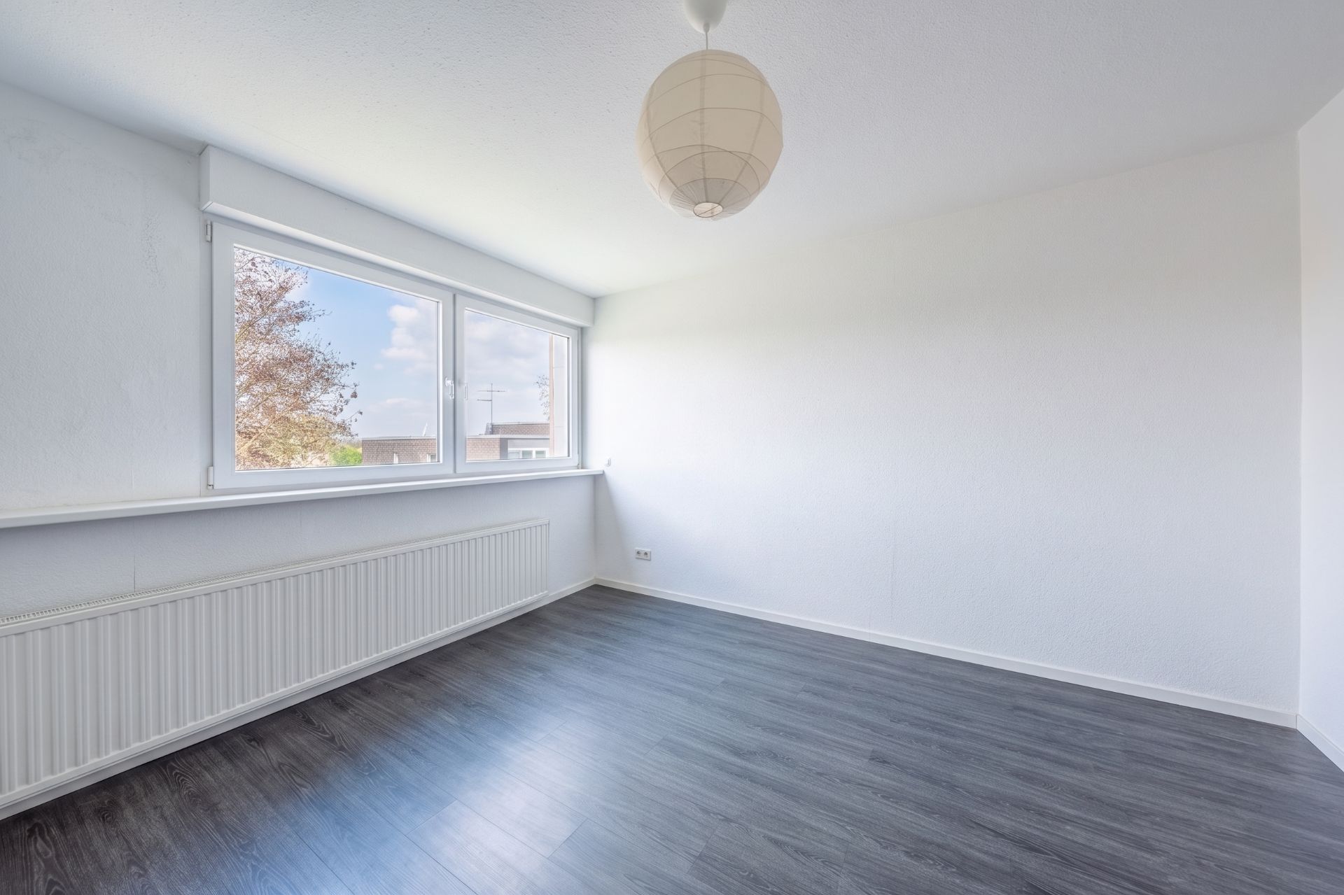Heller Raum mit großem Fenster, dunklem Boden und weißer Wand.