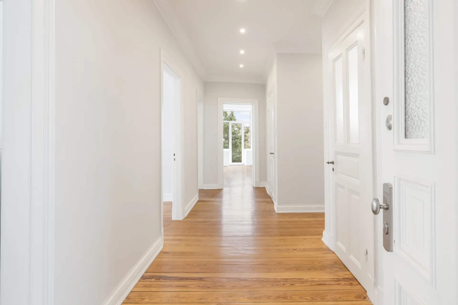 Heller Flur mit Holzboden, weißen Wänden und mehreren Türen in einem Wohnhaus.