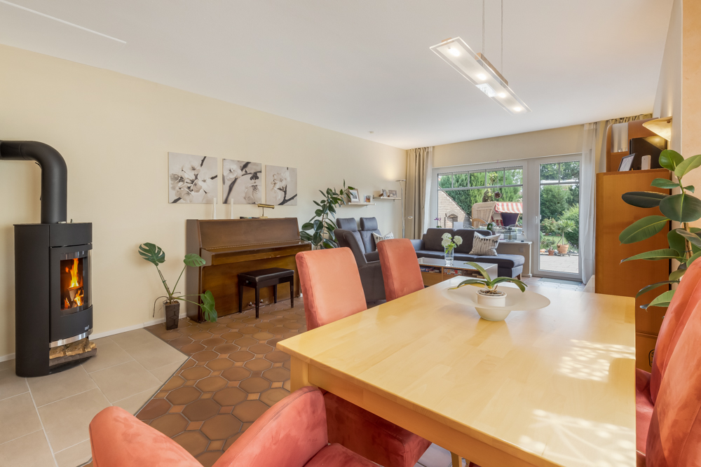 Helles Wohnzimmer mit Kamin, Esstisch, Piano, Sofa und großen Fenstern zum Garten.