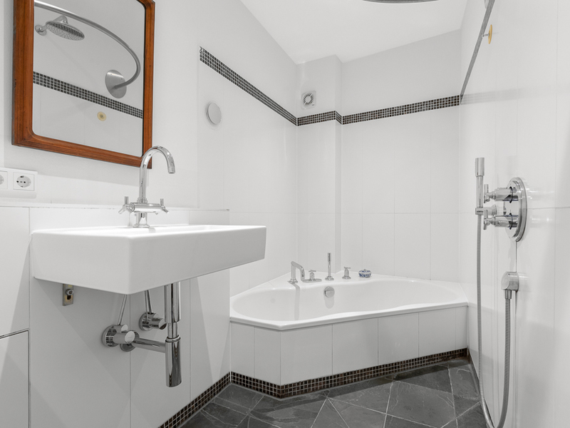 Modernes Badezimmer mit Eckbadewanne, Waschbecken, Spiegel und Dusche mit Handbrause.