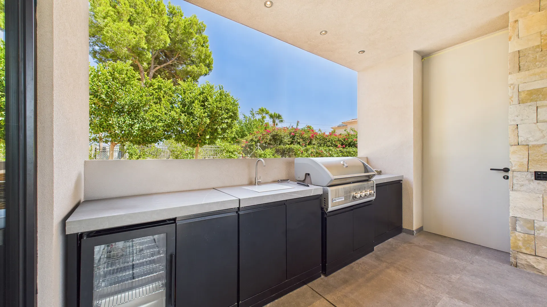 Moderne Außenküche mit Grill, Waschbecken und Kühlschrank, Blick ins Grüne.