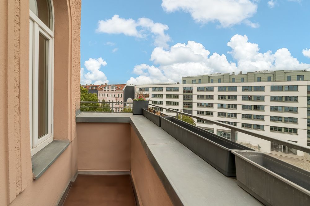 Schmaler Balkon mit Blumenkästen und Blick auf moderne Wohngebäude bei blauem Himmel.