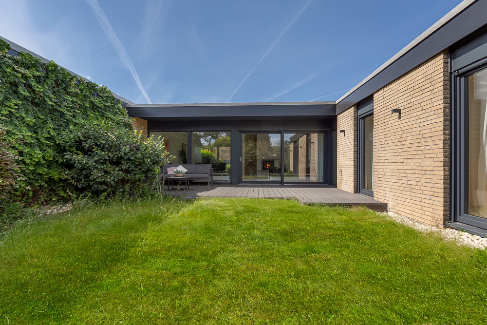 Moderner Backsteinbungalow mit großer Glasfront, Terrasse und gepflegtem Rasen im Innenhof.