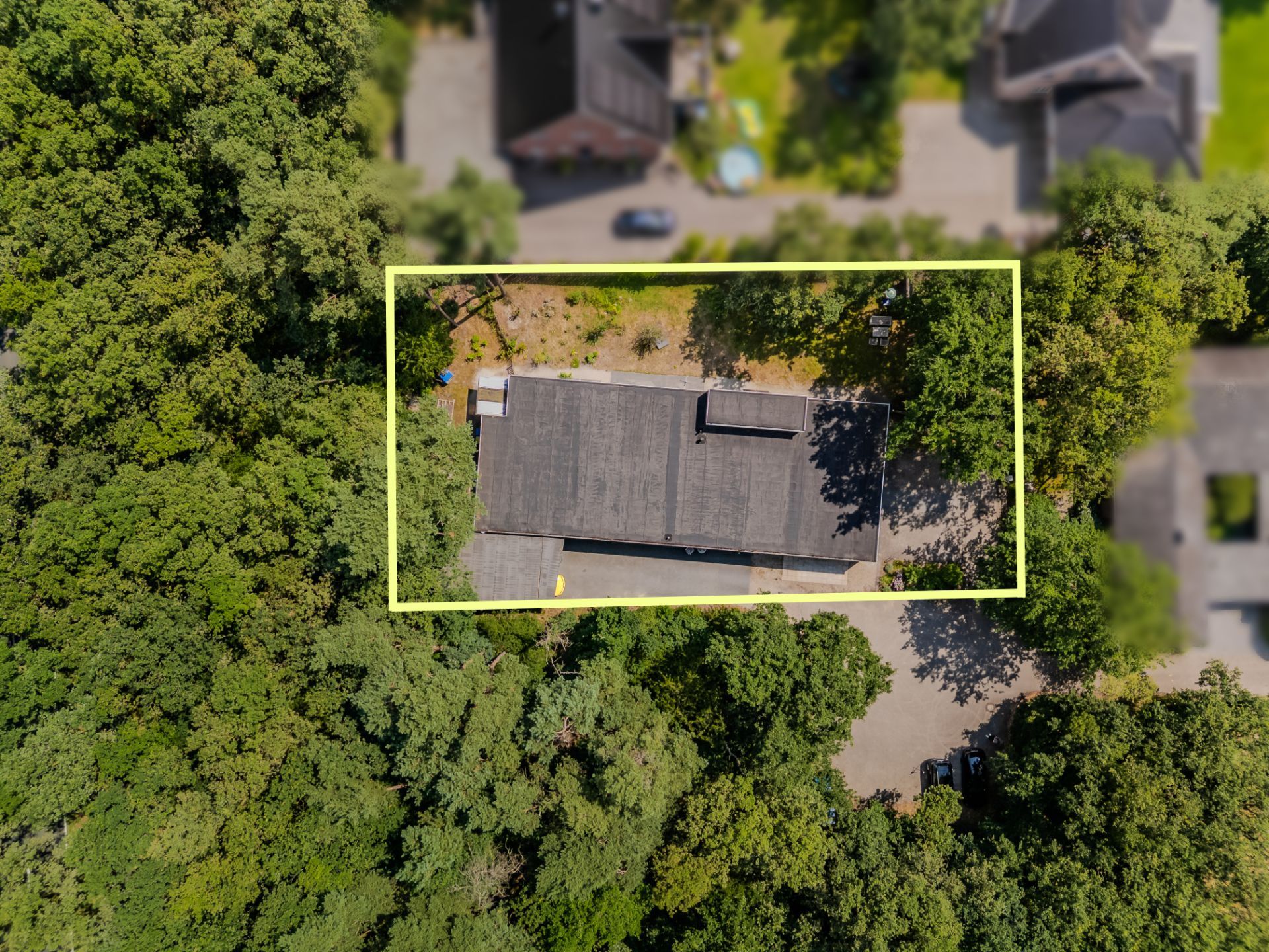Luftaufnahme eines rechteckigen Hauses mit Flachdach, umgeben von Bäumen, gelb markiertes Grundstück.