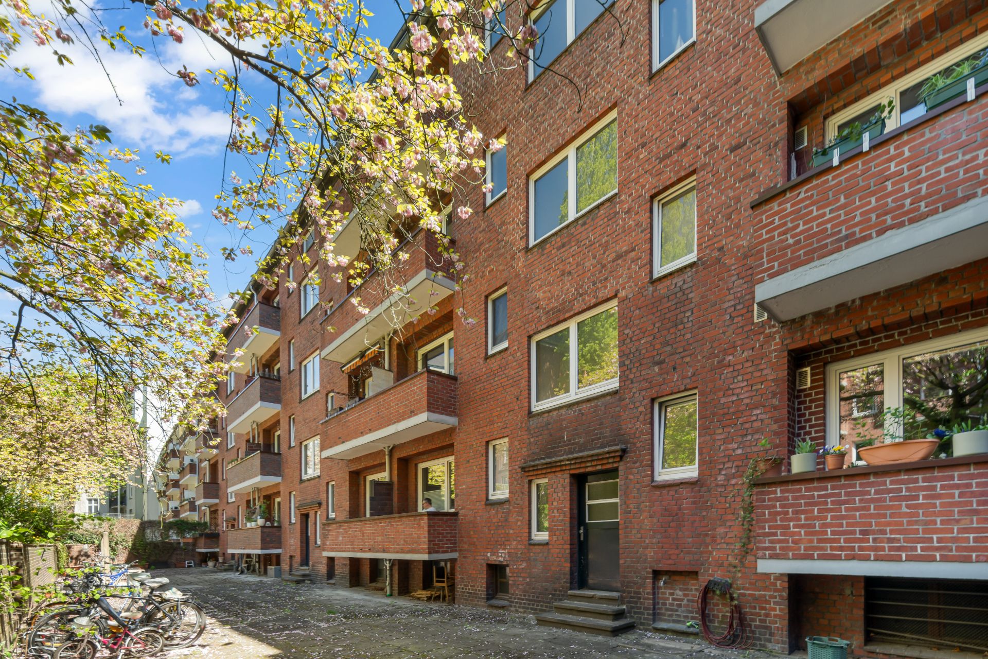 Mehrstöckiges Wohnhaus aus rotem Backstein mit Balkonen und Bäumen davor.