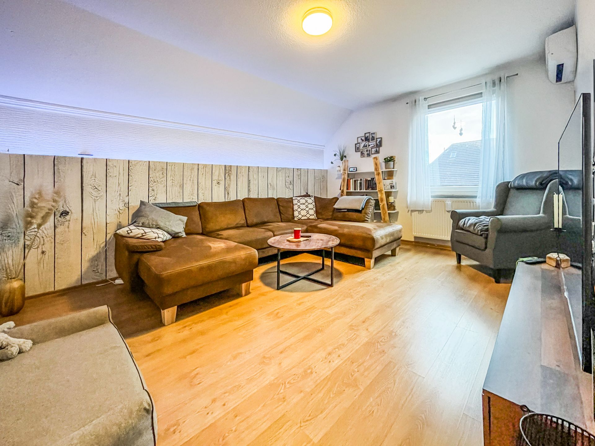 Gemütliches Wohnzimmer mit braunem Ecksofa, Sessel, Couchtisch und Holzfußboden.