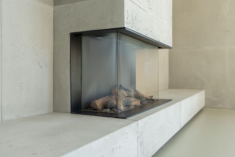Moderner Kamin mit Glasverkleidung und Holzscheiten in einer Ecke eines Wohnraums.