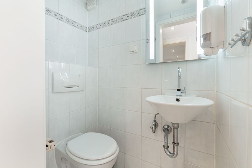 Kleines Badezimmer mit weißer Toilette, Waschbecken und beleuchtetem Spiegel.