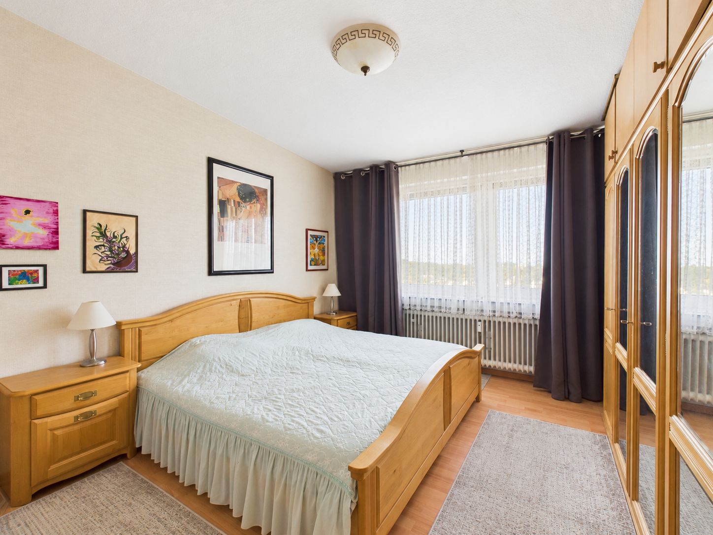Helles Schlafzimmer mit Doppelbett, Holzschränken, großen Fenstern und Bildern an der Wand.
