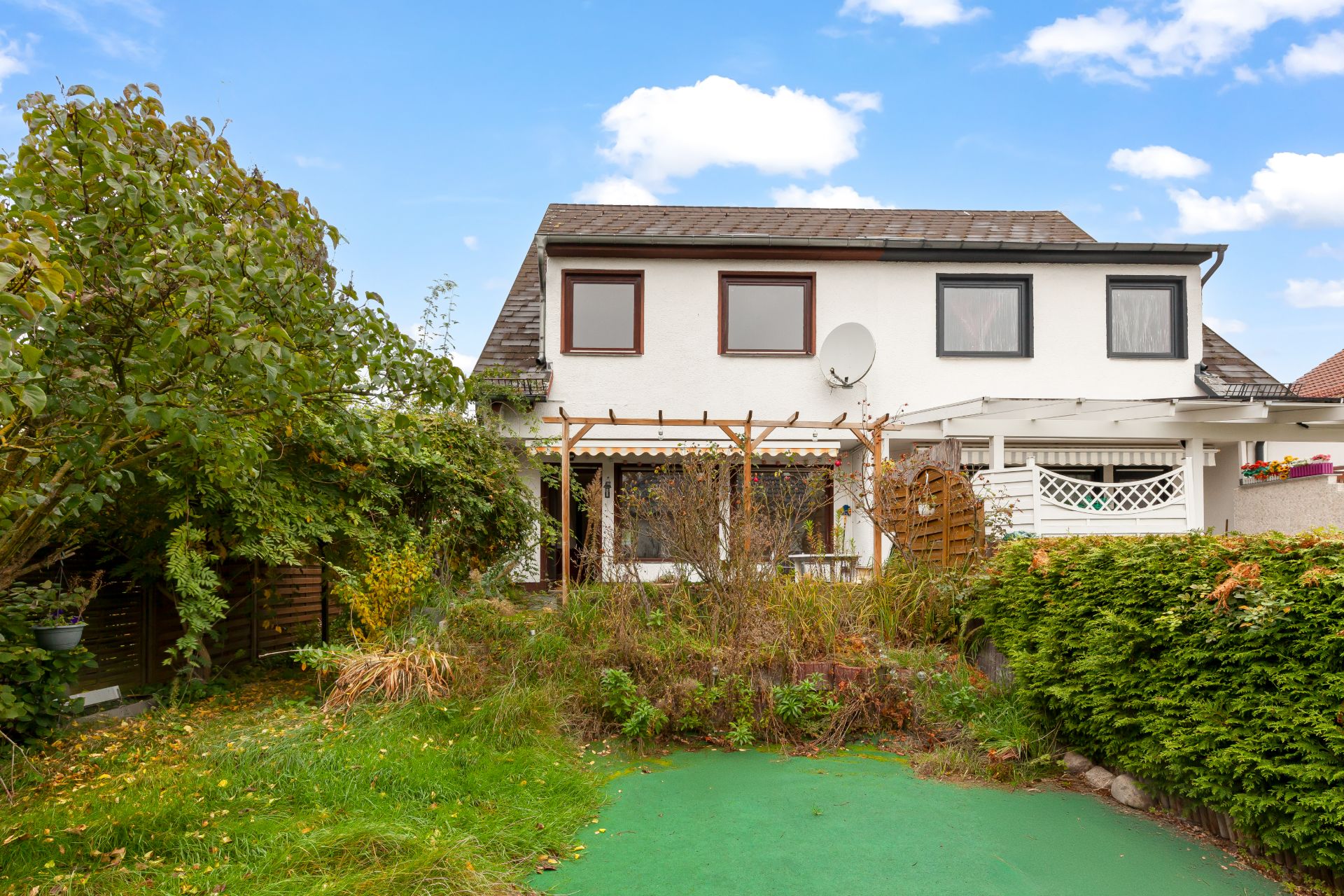 Zweistöckiges weißes Wohnhaus mit großem Garten und Terrasse, umgeben von Büschen und Bäumen.