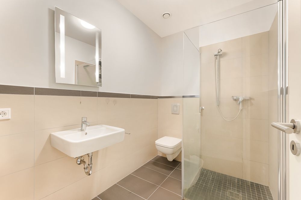 Modernes Badezimmer mit Wandwaschbecken, Spiegel, Toilette und ebenerdiger Dusche.