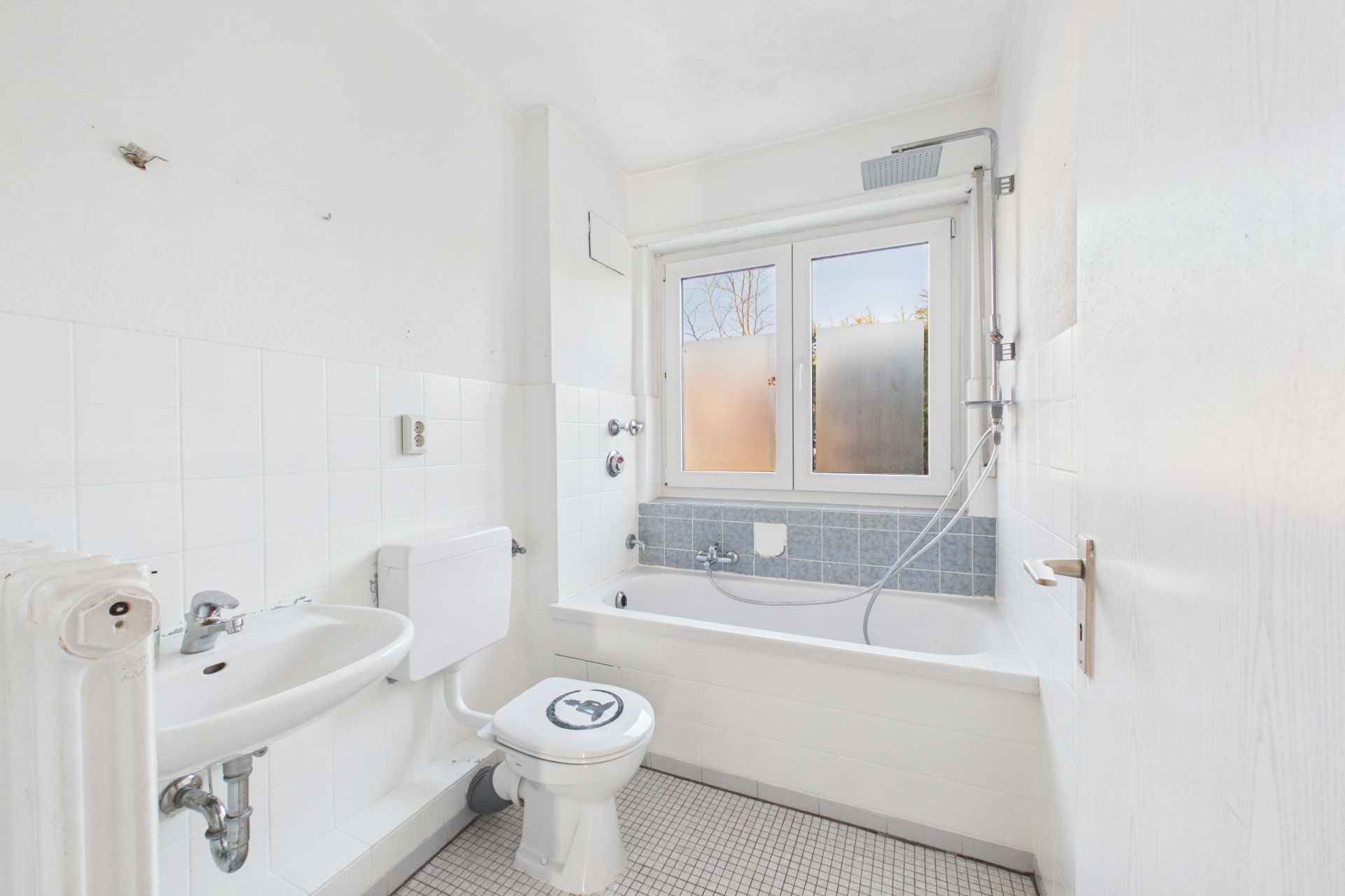 Helles Badezimmer mit Badewanne, Toilette, Waschbecken und Fenster.