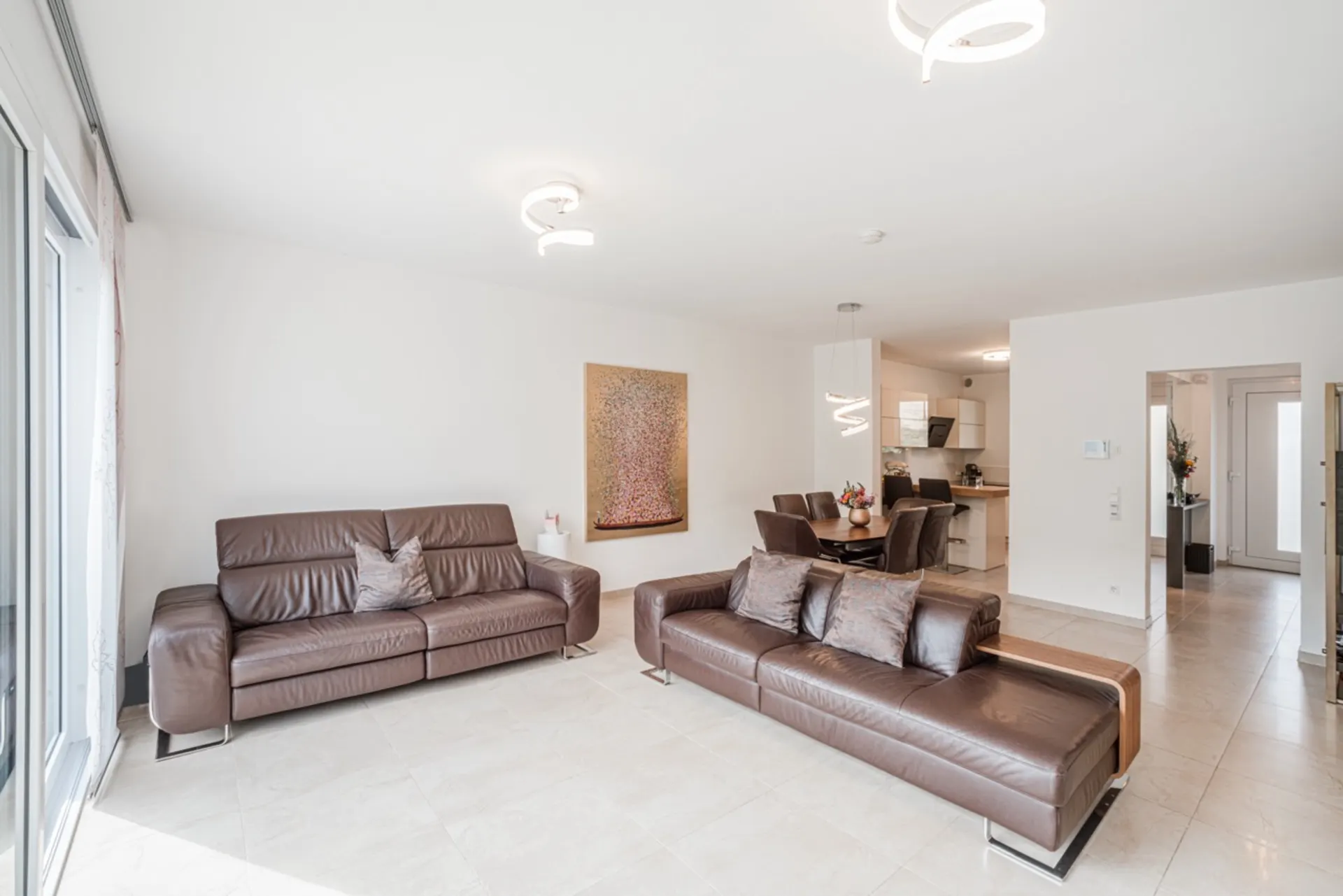 Helles Wohnzimmer mit zwei braunen Ledersofas, Essbereich und offener Küche im Hintergrund.