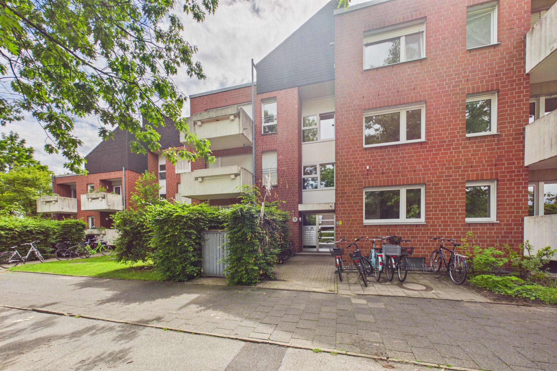 Mehrfamilienhaus mit Backsteinfassade, Balkonen und Fahrrädern vor dem Eingang.