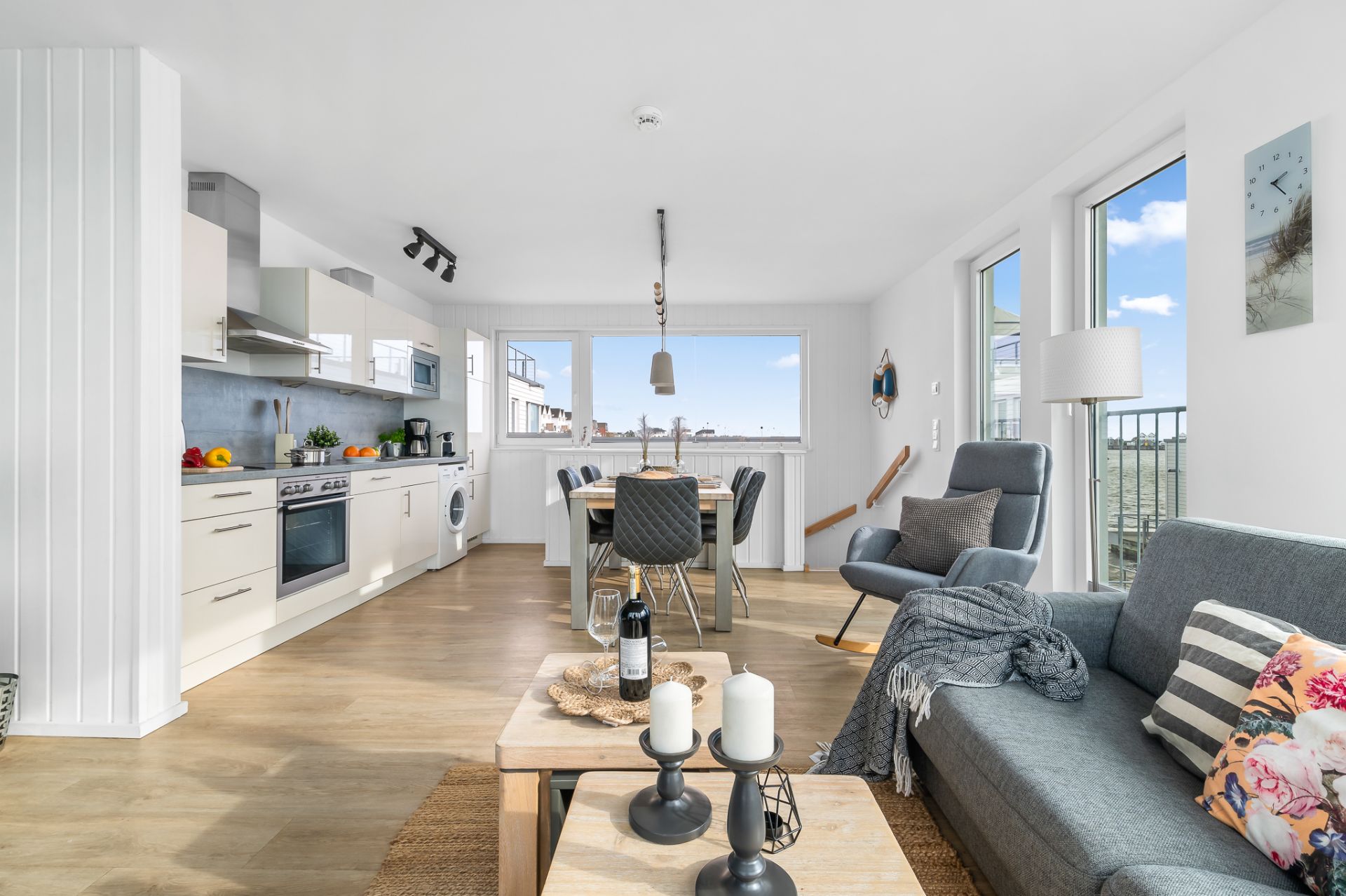 Helles Wohnzimmer mit offener Küche, Esstisch, Sofa, Fenster und Dekorationen.