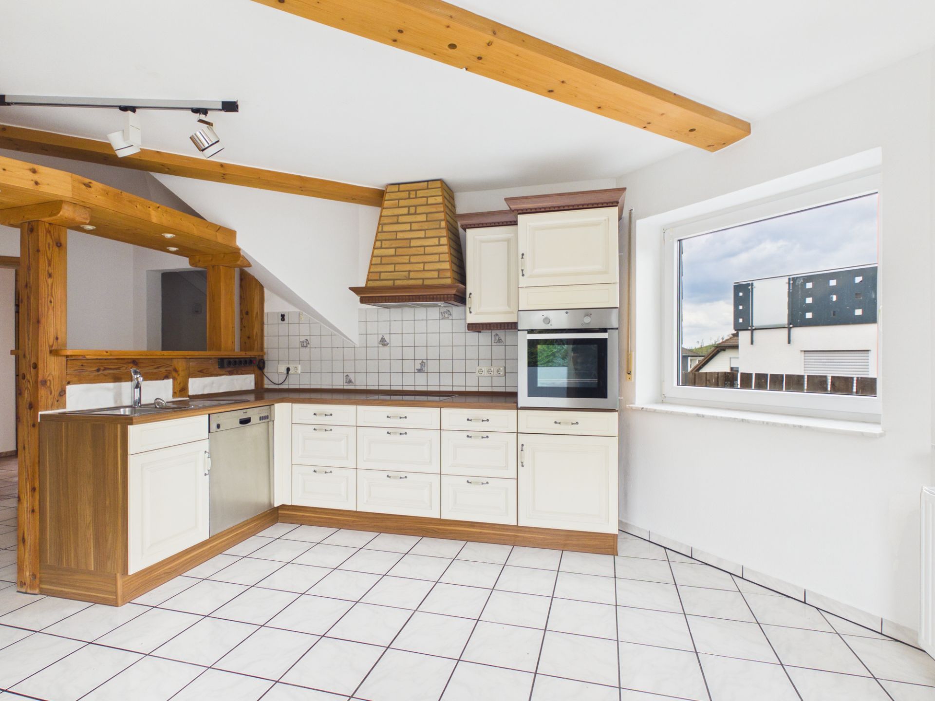Helle Einbauküche mit Holzbalken, weißem Fliesenboden und großem Fenster.