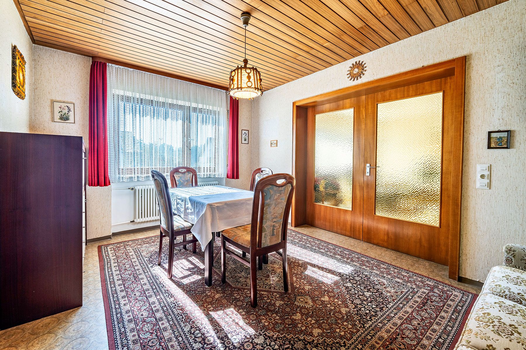 Esszimmer mit Holztisch, vier Stühlen, Teppich und großer Fensterfront.