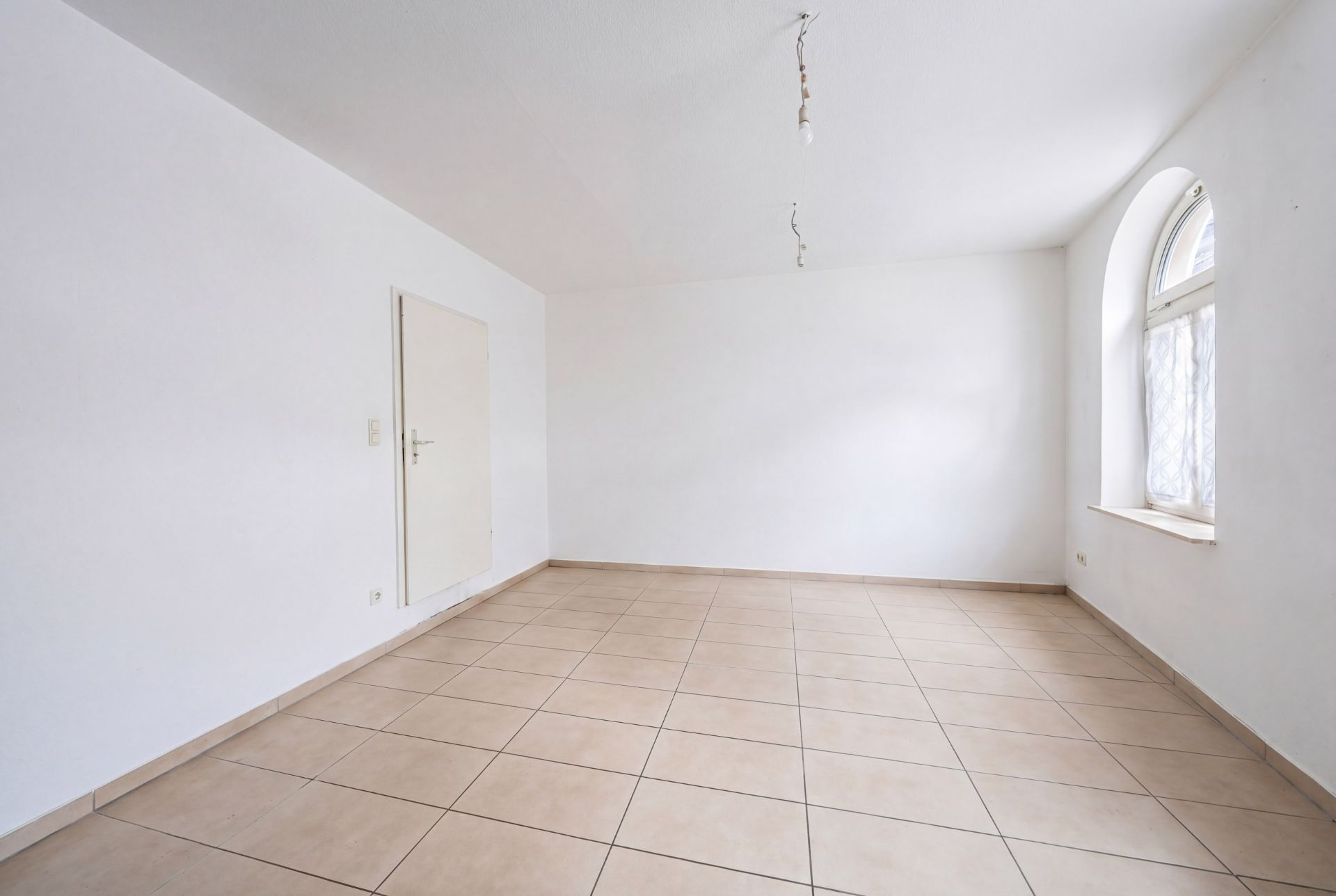 Leerer Raum mit Fliesenboden, weißer Tür und großem Fenster mit Rundbogen.