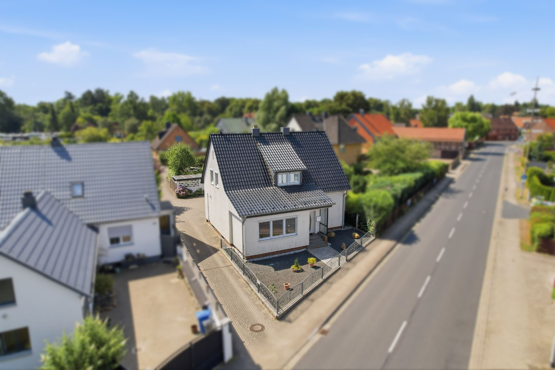 Einfamilienhaus mit Garten und Zaun an einer ruhigen Straße, daneben weitere Wohnhäuser.
