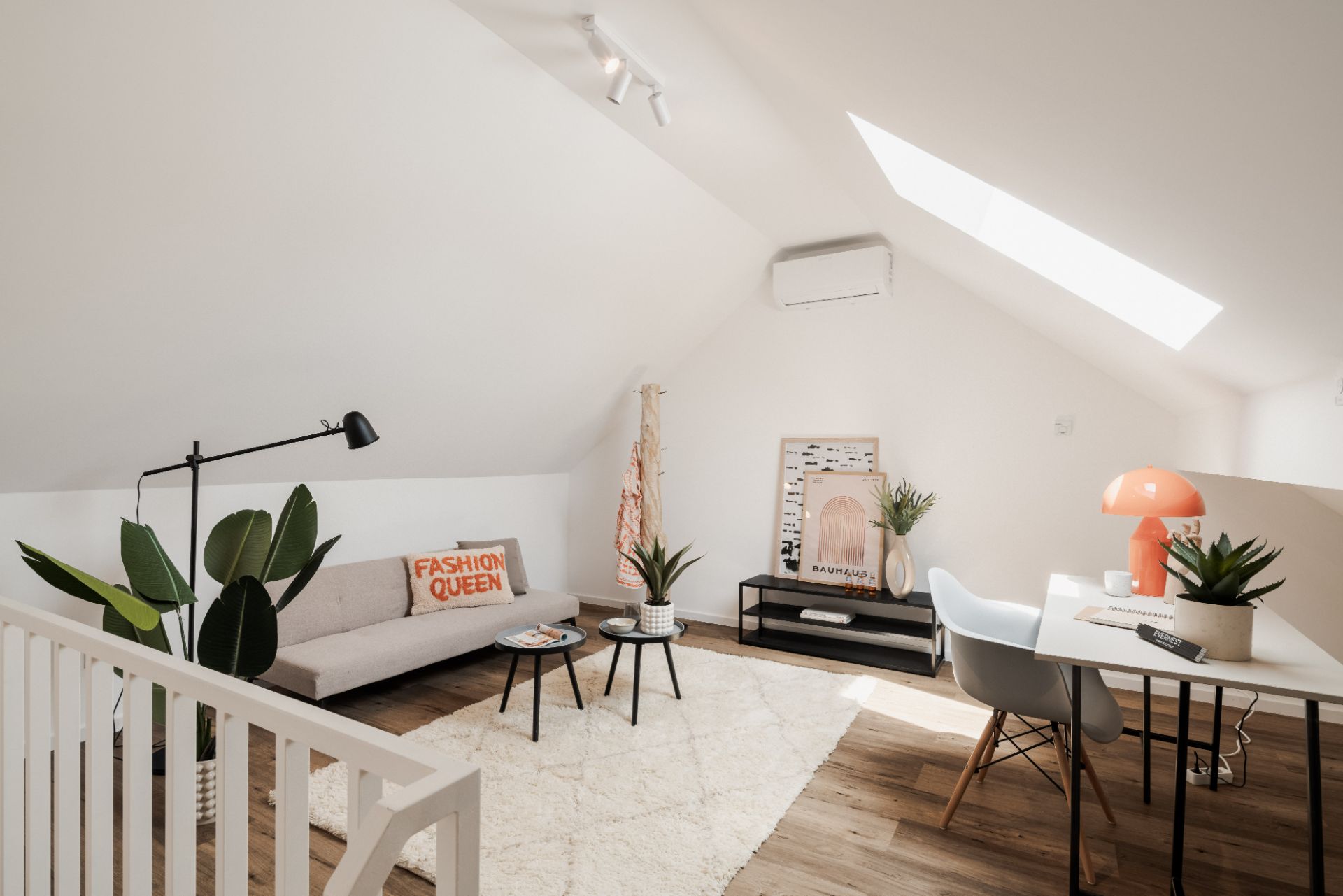 Helles Dachzimmer mit Sofa, Schreibtisch, Pflanzen und Oberlichtfenster.