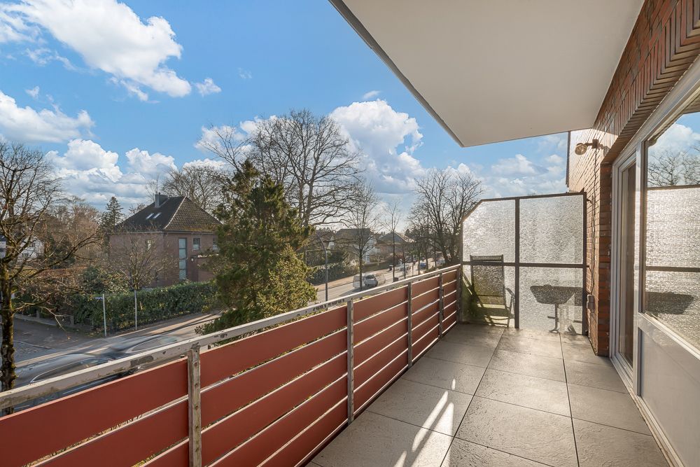Großer Balkon mit Fliesen, rotem Geländer und Blick auf eine ruhige Straße mit Bäumen.