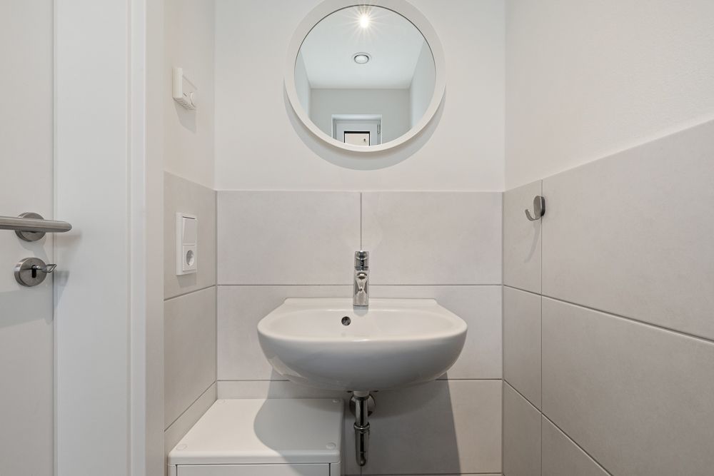 Kleines Badezimmer mit Waschbecken, Spiegel und hellen Fliesen an den Wänden.