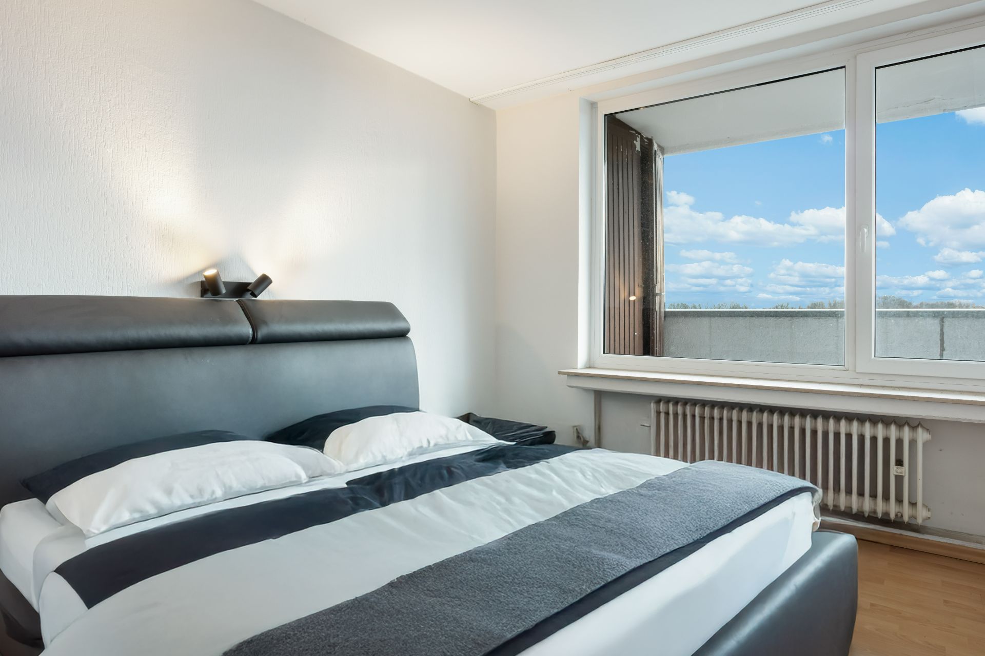 Modernes Schlafzimmer mit Doppelbett, großem Fenster und Blick auf den Himmel.