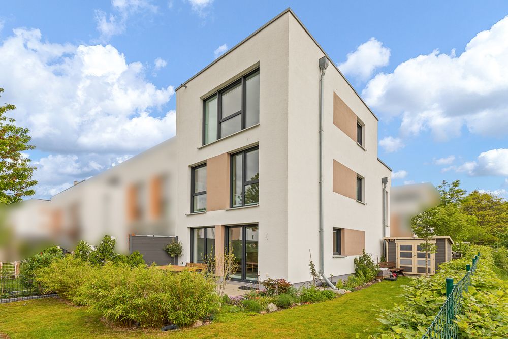 Modernes, weißes dreistöckiges Wohnhaus mit Garten und großer Fensterfront.