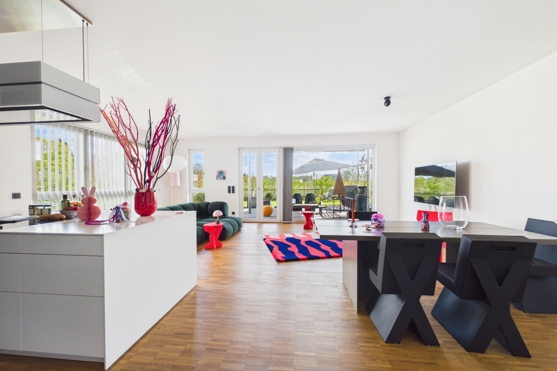 Modernes Wohnzimmer mit offener Küche, Esstisch, Sofa und Zugang zur Terrasse mit Blick ins Grüne.