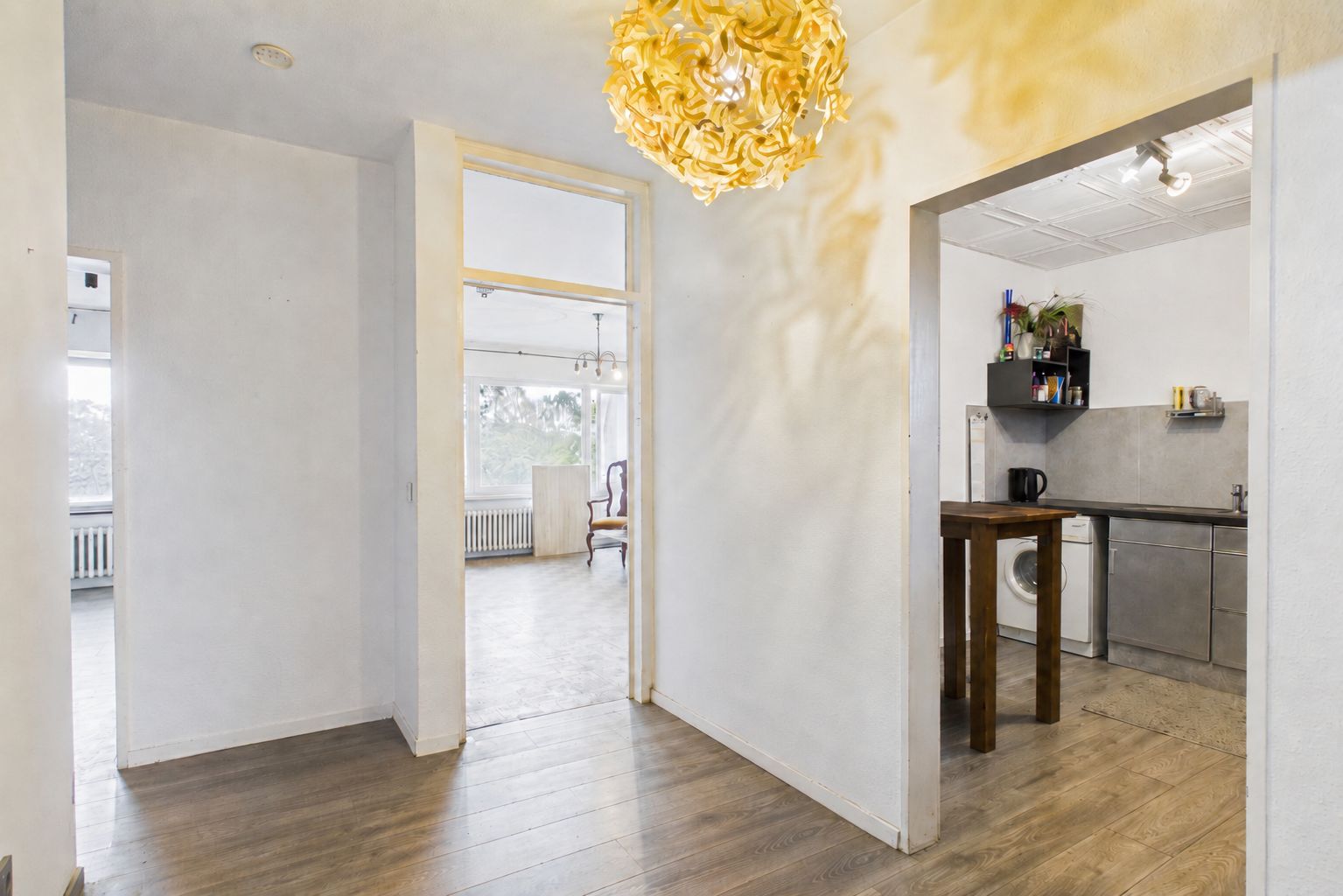 Heller Flur mit Holzfußboden, Zugang zur Küche und zu einem Wohnzimmer mit großen Fenstern.