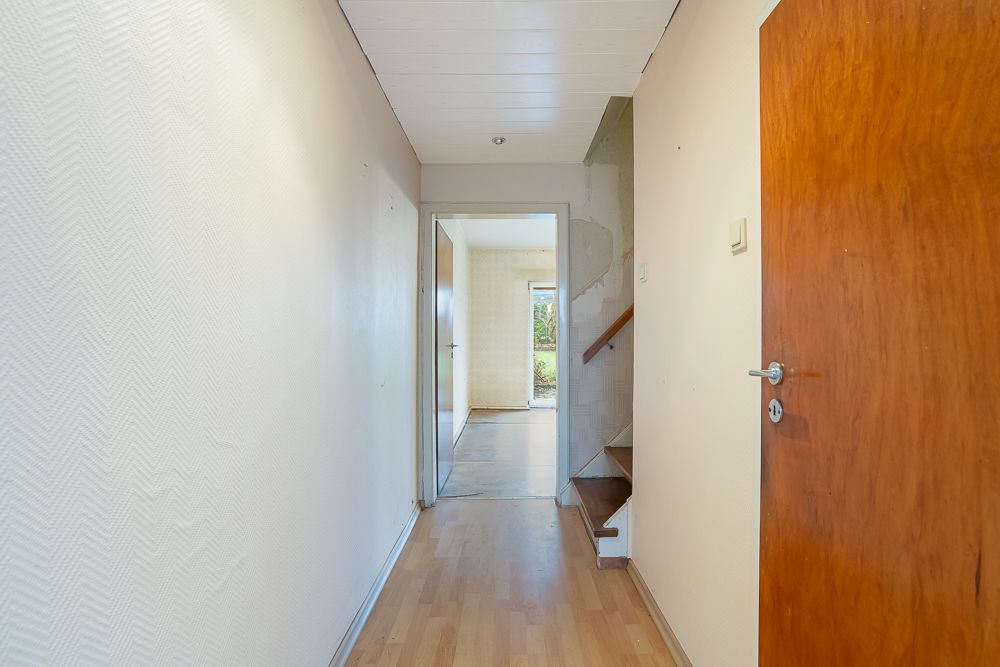 Flur mit Holzboden, offener Tür und Treppe nach oben, Blick in ein weiteres Zimmer.
