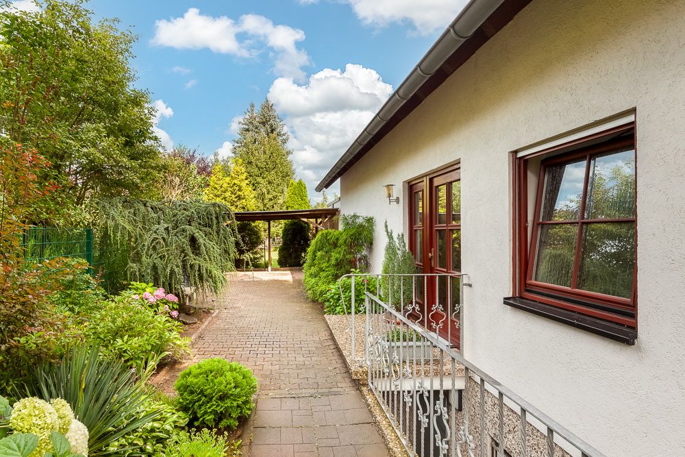 Seitlicher Gartenweg an einem Wohnhaus mit Blumen und Sträuchern bei Tageslicht.