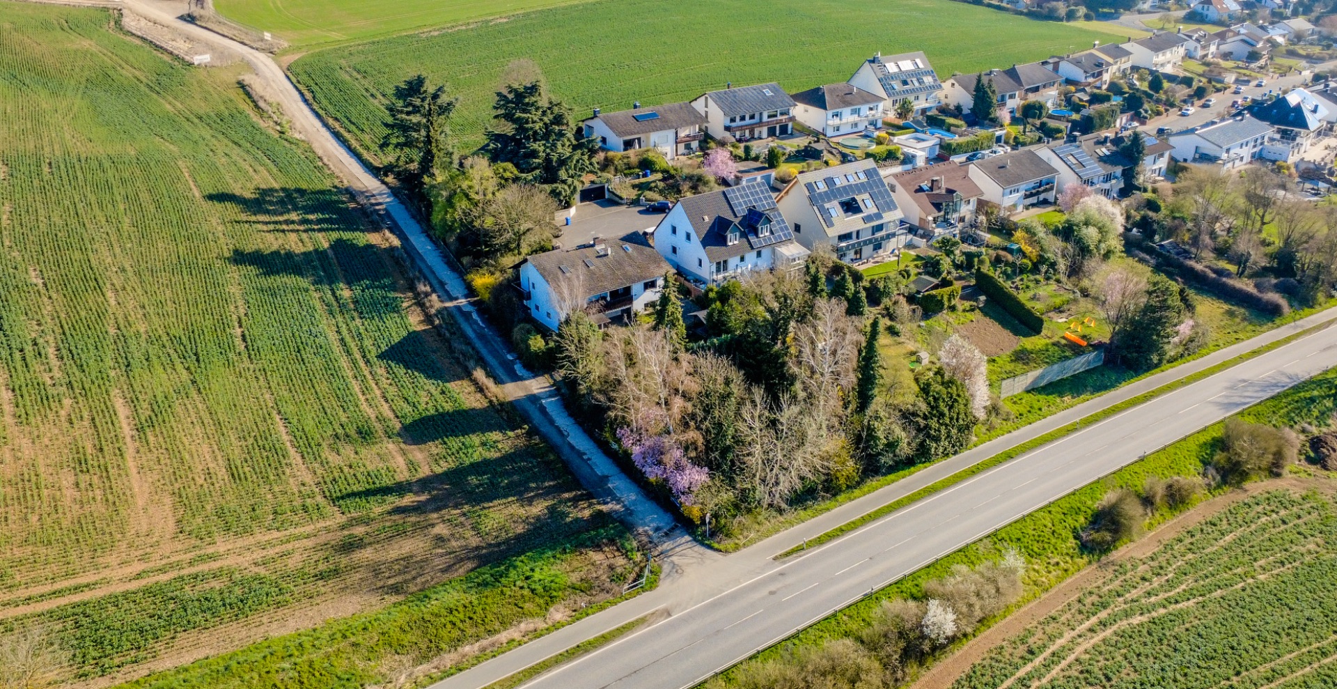 Luftaufnahme von Wohnhäusern am Rand eines Feldes, von Straßen umgeben.